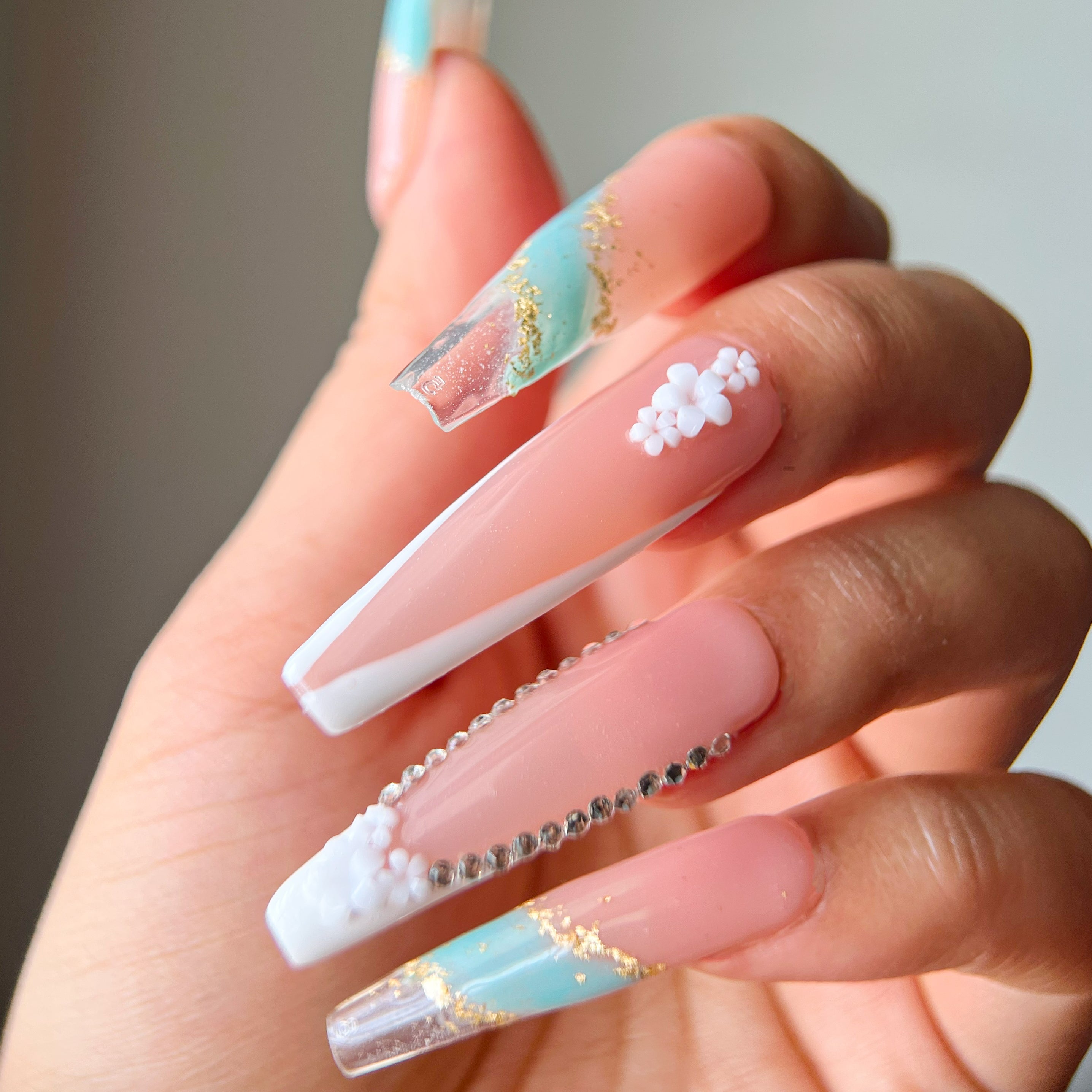 Long coffin press-on nails featuring gold, olive, and marble tones with white reverse French tips and floral gem accents for a bold, elegant look.